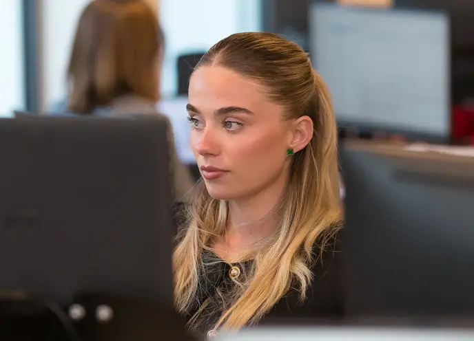 A young woman with a serious expression looking at a computer screen in a modern office.
